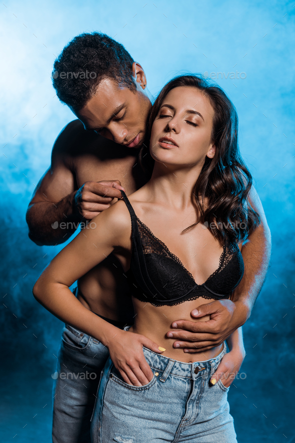 handsome bi-racial man touching lace bra of sexy girl on blue with