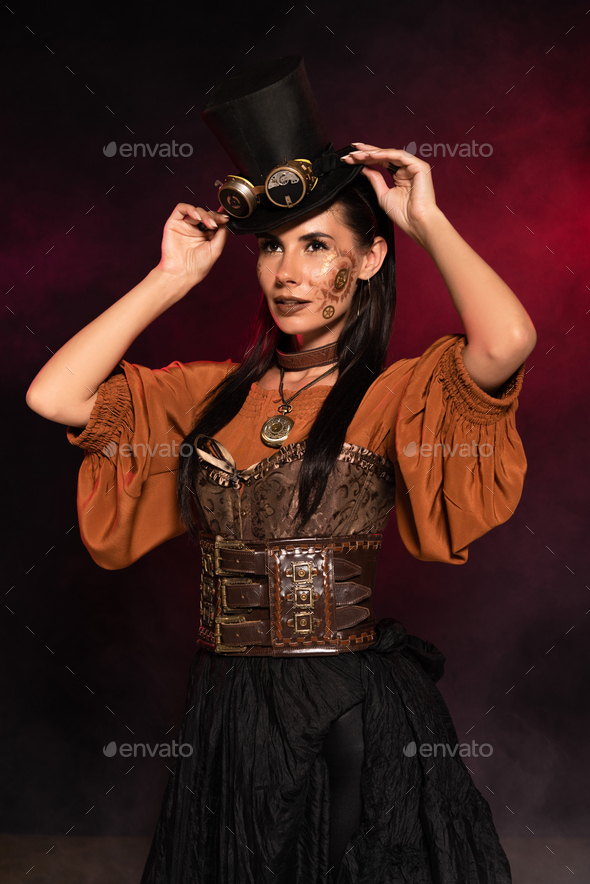 attractive steampunk woman with makeup putting on top hat on black in pink smoke