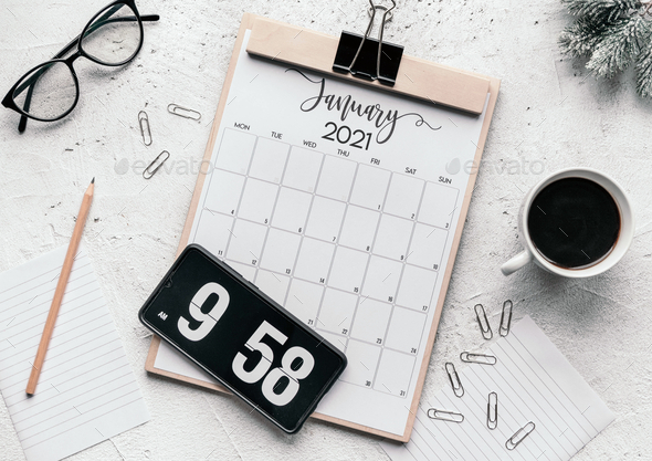 Flat lay of a calendar diary, flip clock screensaver on the phone, mug, glasses, clips, and pencil