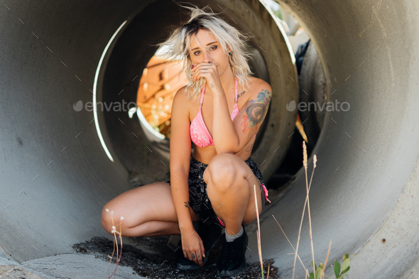 Young caucasian tattooed female with white hair posing squatted on the tubes