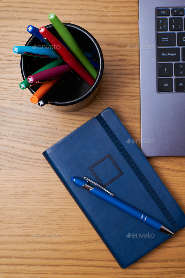 Vertical shot of a pen on a journal, pen box, and laptop on a wooden table