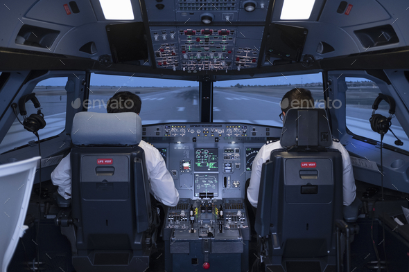 Two pilots in the cockpit of a commercial flight simulator preparing to start the flight