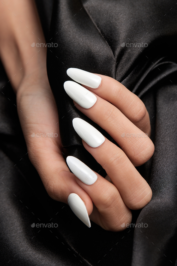 Female hand with long white nails holding a black satin fabric Stock Photo  by wirestock