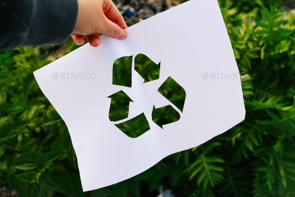 hand holding cut paper with the logo of recycling on dump garbage trash background. Recycling concep