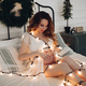 Charming pregnant woman poses for the camera in white dress on the bed with a lor of lights - PhotoDune Item for Sale