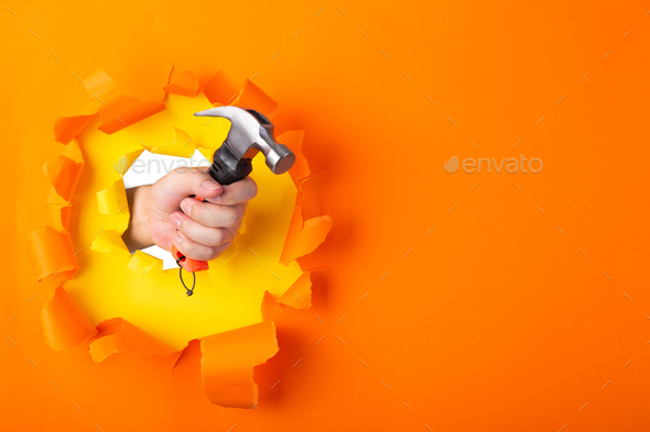 hand with hammer through a torn orange paper