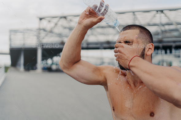 athletic guy with muscular body pours water on himself from bottle, recovers after hard workout