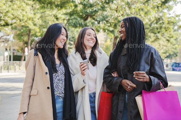 Three multiracial happy young women walking and talking on a shopping day. Group of girls carrying - Stock Photo - Images
