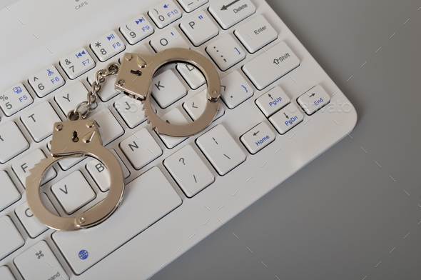 Laptop keyboard and handcuffs isolated on a grey background. Online scam, hacking. fraud, arrest