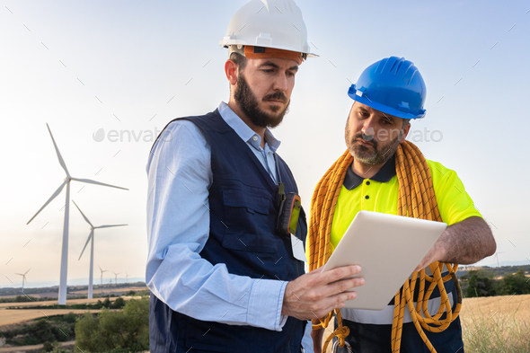 Engineer and wind turbine farm maintenance worker looking together plans in digital tablet. - Stock Photo - Images
