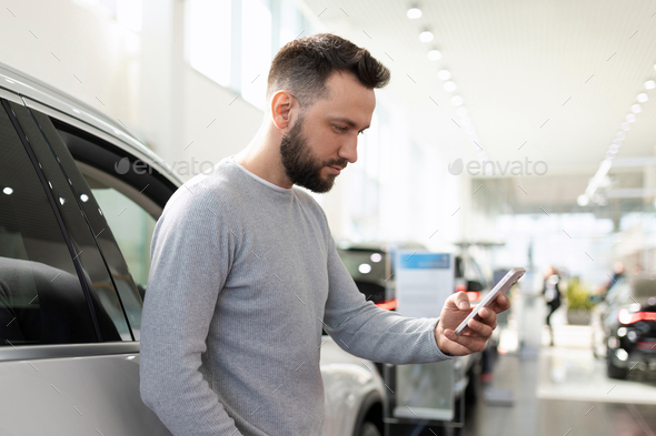 the buyer in the dealership auto center chooses a car compares prices in a smartphone via the