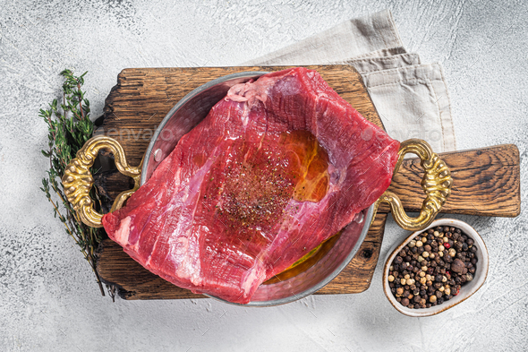Flap or flank steak, raw beef meat in skillet with herbs and olive oil. White background. Top view