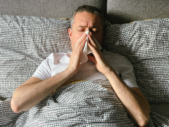 Middle aged man is sick at home, having flu or hangover. Middle aged man is in bed having flu covid