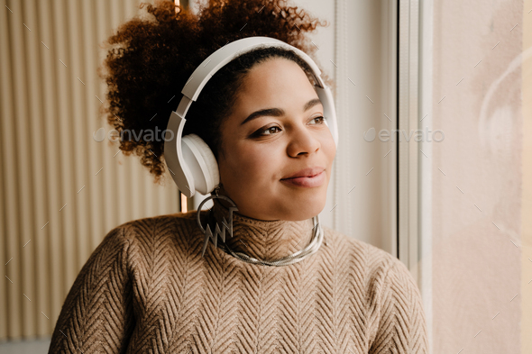 African american woman wearing headphones looking out window at home - Stock Photo - Images
