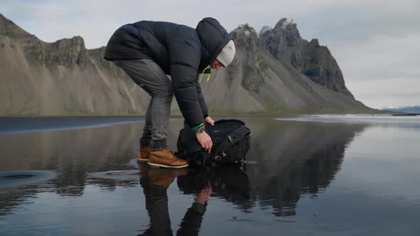 Hiker Arranging Backpack With Tripod On Wet Beach alt