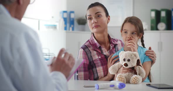 Pediatrician Using Clipboard While Examining Little Girl with Her Mother in Clinic Office alt