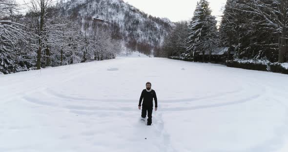 Backward Aerial Over Man Walking with Snowshoes on Snow Covered Field Near Pine Forest Woods in