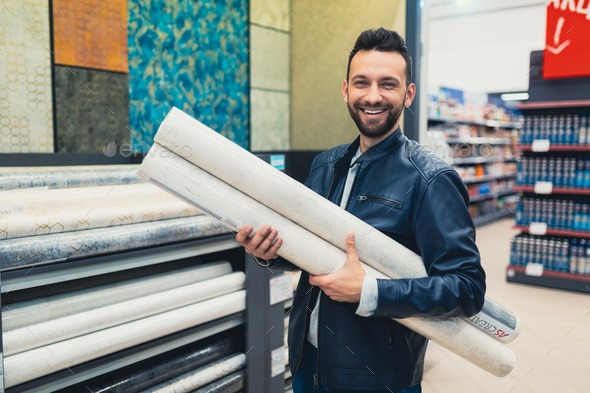 satisfied customer in a hardware store with rolls of wallpaper in his hands looking at the camera