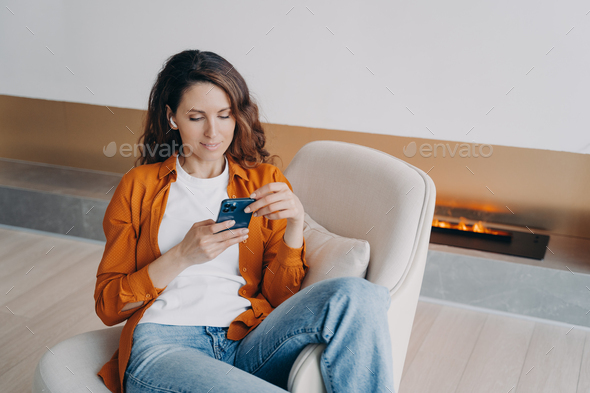 Modern girl in earphones using smartphone apps, shopping online, listening to new podcast or music