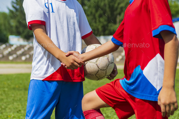 A close-up of the cut off arms of two young footballers. Handshake before the start of the match.