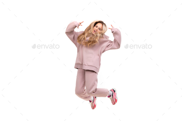 beautiful charismatic blonde in a pink tracksuit jumps on a white background, photo in a jump