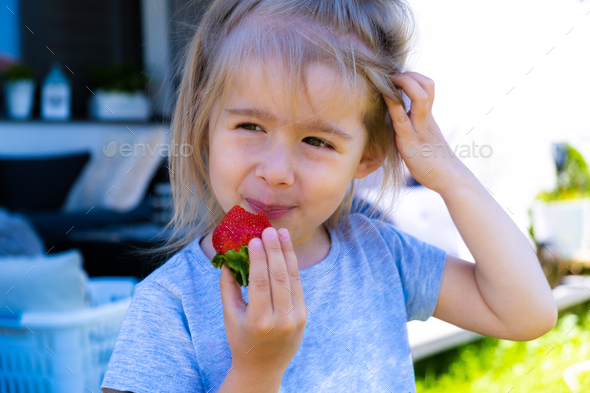 little blonde girl eating fresh strawberry - Stock Photo - Images