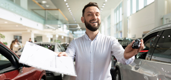car dealership worker handing keys and documents from a new car to a happy buyer