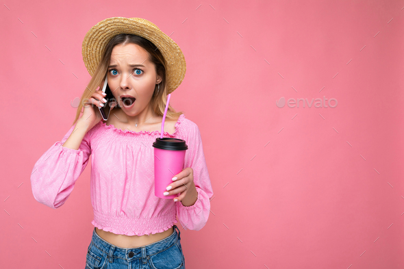 Photo of beautiful surprised emotional young blonde woman wearing pink crop blouse and straw hat