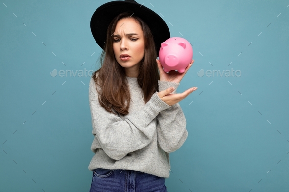 Portrait of thinking angry young beautiful pretty brunette woman wearing gray pullover and black hat