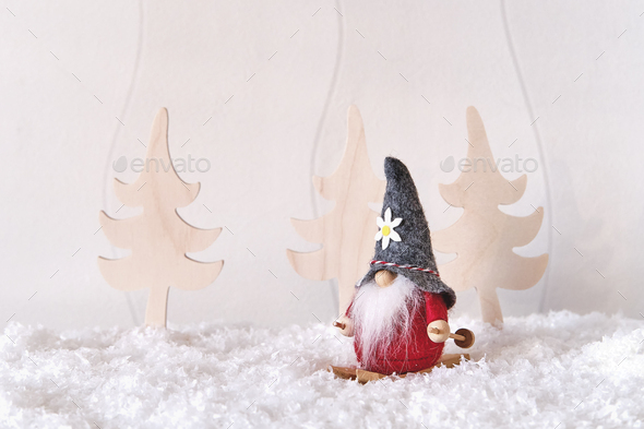 Christmas composition. Christmas gnome on skiing, fir trees, artificial snow, white wall.