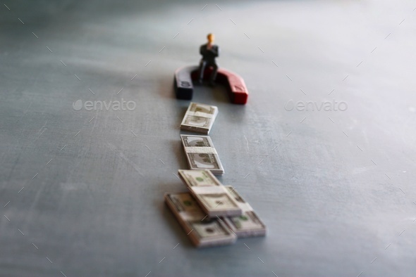 Selective focus image of miniature businessman attracts money using magnet