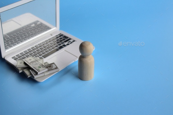Wooden doll in front of laptop and pile of money