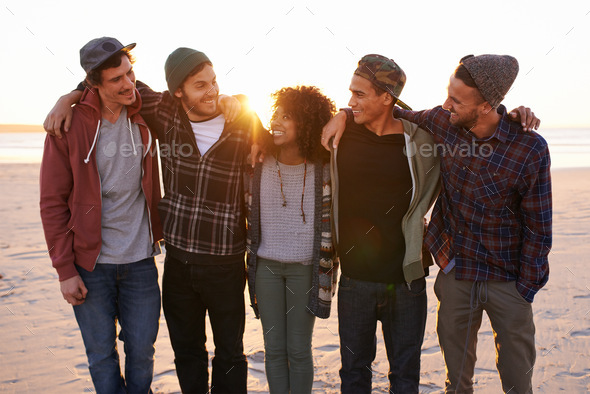Friends make the world a better place. Shot of a group of friends walking along a beach at sunset.