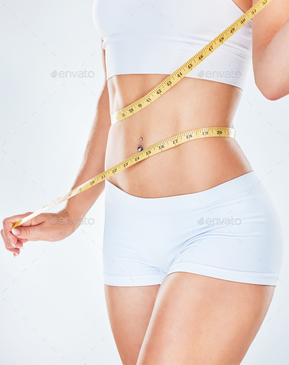 Body, tape measure and diet with a woman measuring her waist to track  weightloss in studio on a gra Stock Photo by YuriArcursPeopleimages