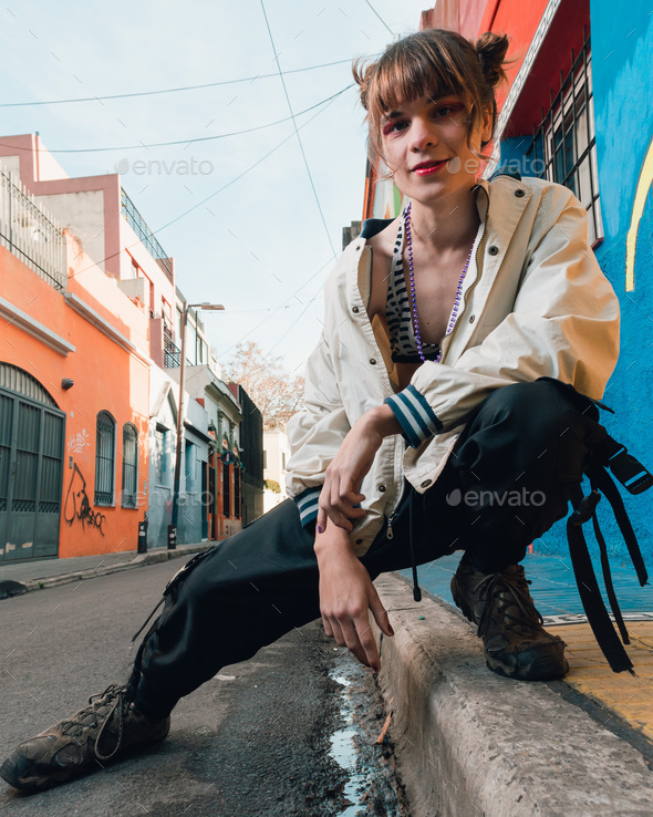 trans latin young woman posing looking at the camera crouched on the edge of the sidewalk