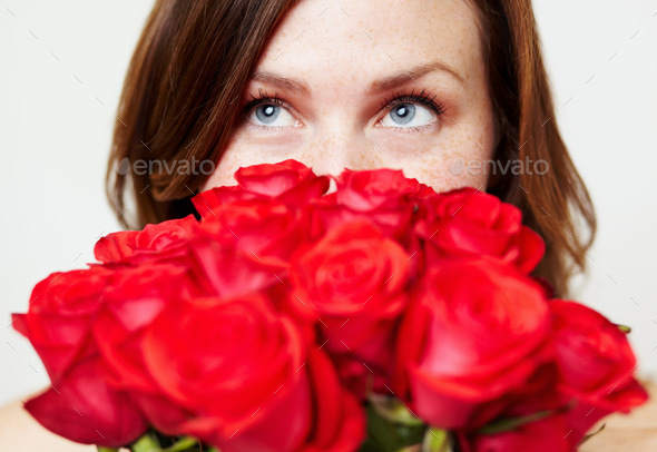 Thinking about that special someone. An attractive young woman peering over a bouquet of roses.