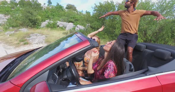 Three multi ethnic friends partying in red convertible parked on side of road alt