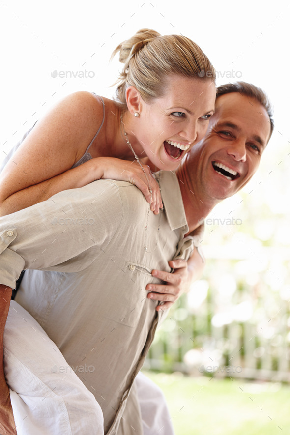A cropped shot of a happy man and woman laughing while he gives her a piggyback ride