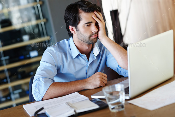 A frustrated employee sitting at his desk and working on his laptop