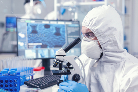 Concentrated scientist in ppe equipment looking into the microscope ...