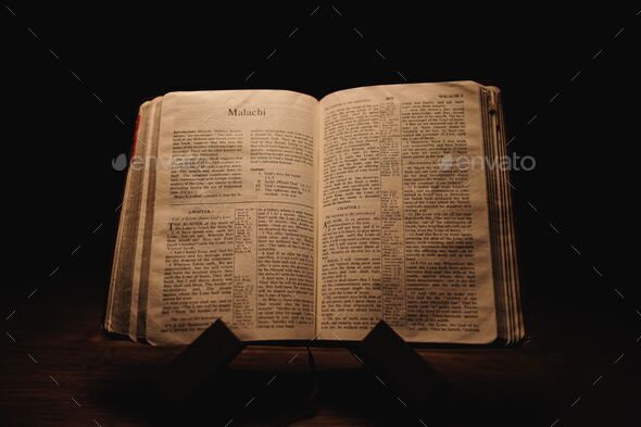 Closeup shot of a historic old Bible open on the Malachi pages on display  in a dark room Stock Photo by wirestock