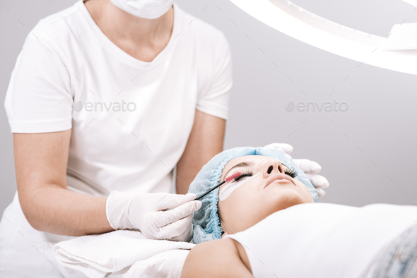 eyelash master brushing false eyelashes on model face during procedure isolated on grey
