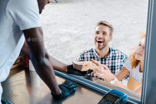 cropped view of african american man giving carton plate with hot dog to customers