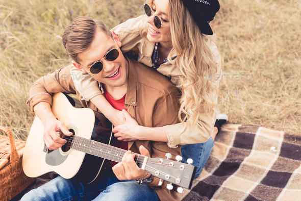 handsome man playing acoustic guitar and attractive woman hugging him ...