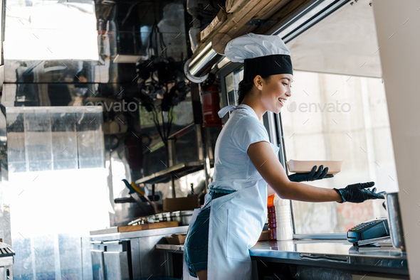 happy asian woman in latex gloves holding carton plate in food truck