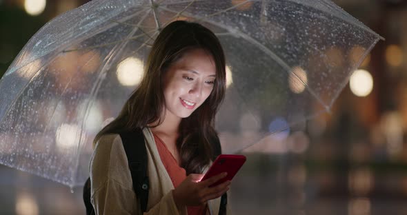 Woman use of mobile phone and hold with umbrella in the evening alt