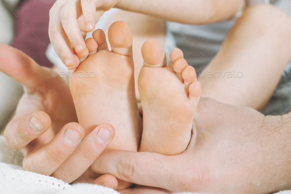 Children\'s feet in hands of father, dad tickles feet of kid. Baby counts toes
