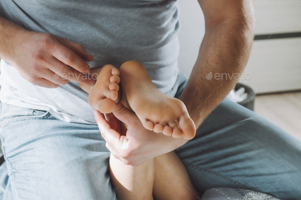 Children's feet in hands of father. Dad tickles feet of kid sitting on them. Family, having fun at