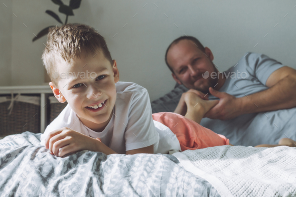 Father plays with his son 7-10 on bed. Dad tickles kids feet. Family, having fun