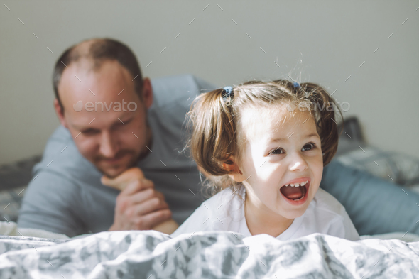 Father plays with little daughter 2-4 on bed. Dad tickles kids feet with his beard. Family, having